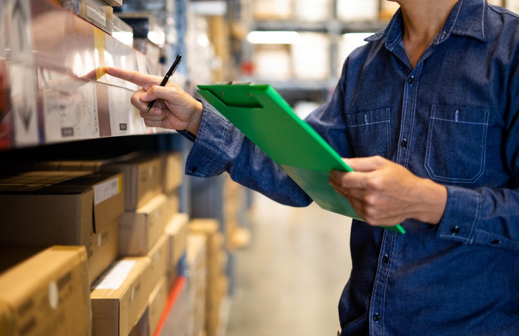 Manager man worker doing stocktaking of product management in cardboard box on shelves in warehouse. Physical inventory count."n Male professional assistant checking stock in factory.